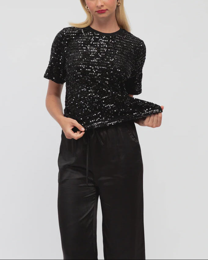 Woman wearing a black sequin top and black pants on a light gray background